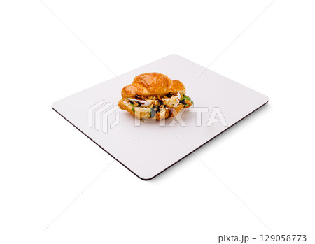 Gourmet croissant filled with savory ingredients on a clean surface 129058773