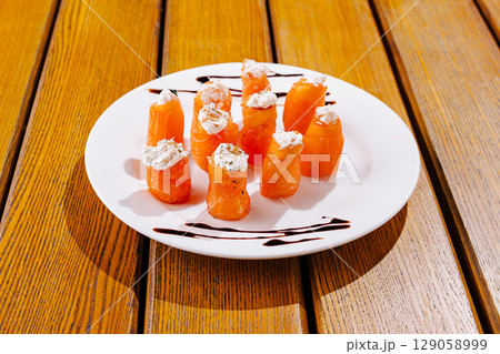 Colorful salmon rolls topped with cream cheese sit artfully on a white plate Colorful salmon rolls topped with cream cheese sit artfully on a white plate 129058999