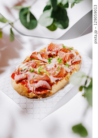 Delicious flatbread topped with meats and herbs presented on a light background Delicious flatbread topped with meats and herbs presented on a light background 129059013