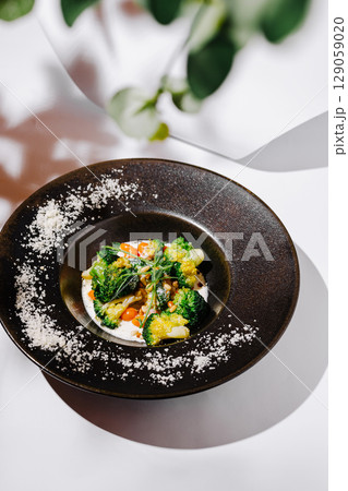 Colorful vegetable dish served in an elegant black bowl on a white table 129059020