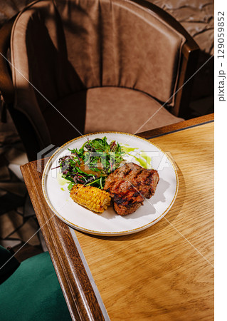 Grilled meat with salad and corn served on a plate in a cozy restaurant Grilled meat with salad and corn served on a plate in a cozy restaurant 129059852