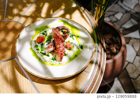 Octopus dish served on a wooden table in a bright, tropical setting 129059888