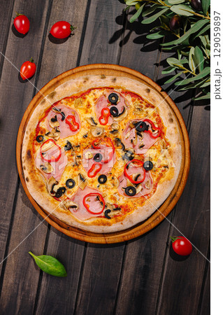 Delicious pizza topped with ham, olives, and bell peppers on wooden table 129059897
