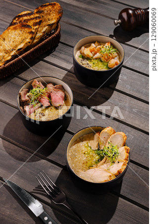 Rustic risotto bowls with chicken, beef, and shrimp, served with toasted bread and herbs 129060069