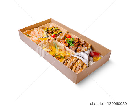 Delicious variety of grilled meats, vegetables, and garnishes in a takeout box 129060080