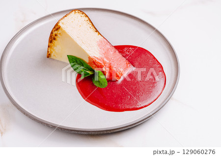 Delicious cheesecake slice garnished with raspberry sauce and mint Delicious cheesecake slice garnished with raspberry sauce and mint 129060276