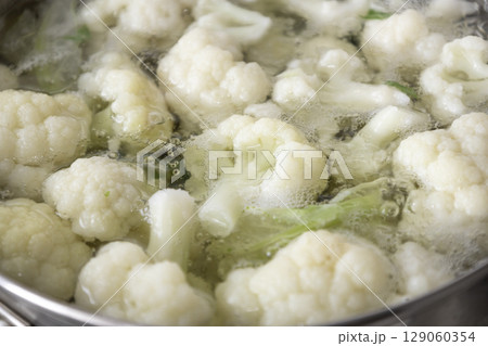 Fresh cauliflower is boiled in a saucepan with water. The vegetable is divided into florets and boiled in a saucepan. Fresh cauliflower is boiled in a saucepan with water. The vegetable is divided into florets and boiled in a saucepan. 129060354