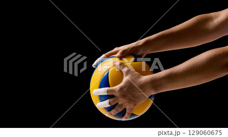 Hands holding blue and yellow volleyball against black background Hands holding blue and yellow volleyball against black background 129060675