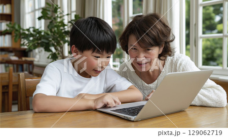 Asian boy and woman engaged in learning together at a wooden table with laptop and plants Asian boy and woman engaged in learning together at a wooden table with laptop and plants 129062719