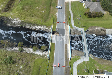 Repair of destroyed bridge after hurricane flood in Florida. Reconstruction of damaged road after flooding water washed away asphalt. Police car at roadwork site 129062791