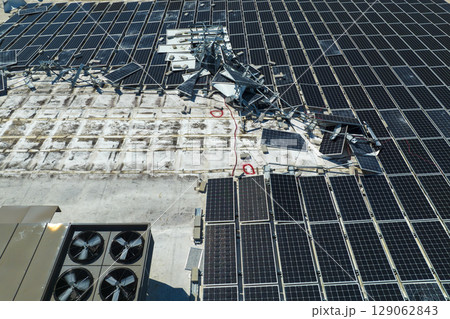 Photovoltaic solar panels destroyed by hurricane strong wind mounted on industrial building roof for producing green ecological electricity. Consequences of natural disaster in Florida Photovoltaic solar panels destroyed by hurricane strong wind mounted on industrial building roof for producing green ecological electricity. Consequences of natural disaster in Florida 129062843