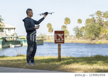 Operator is preparing to fly his quadcopter in national park no drone area. Man unlawfully using his UAV near restriction notice sign 129062856