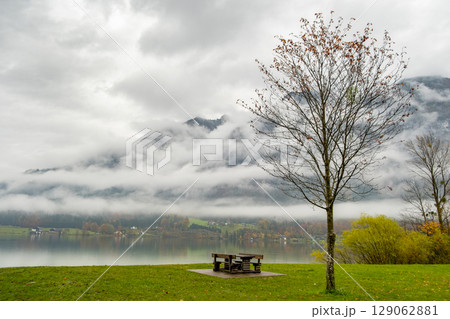 Moody autumn landscape with bare tree and lonely bench on mountain lake shore. Moody autumn landscape with bare tree and lonely bench on mountain lake shore. 129062881