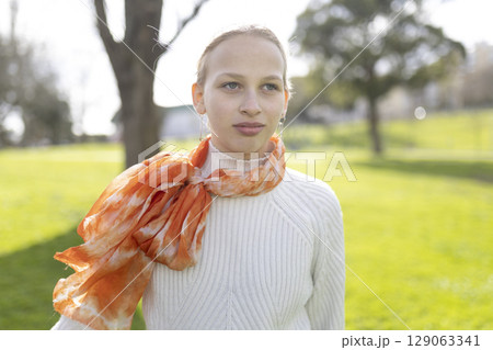 Young person wearing orange scarf and white sweater in park 129063341