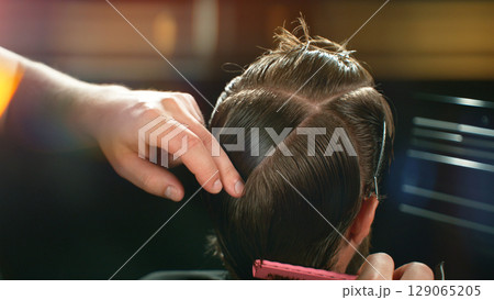 Young Man with Beard at Barber Shop. Barber is Preparing his Haircut. Dark Atmosphere, Black Background. Concept of Barber and a Client. Young Man with Beard at Barber Shop. Barber is Preparing his Haircut. Dark Atmosphere, Black Background. Concept of Barber and a Client. 129065205