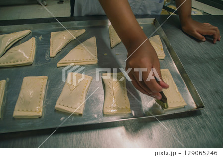 A baker prepares pastries on a tray, showcasing the art of pastry-making in a kitchen environment. A baker prepares pastries on a tray, showcasing the art of pastry-making in a kitchen environment. 129065246