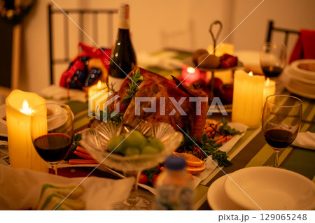A cozy dining table setting with candlelight, wine, and a delicious festive meal ready to be enjoyed. 129065248