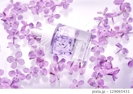 A bottle of hyaluronic serum in lilac flowers in the water. 129065431