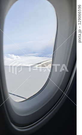 View from airplane window showing aircraft wing above white clouds under a blue sky 129066596