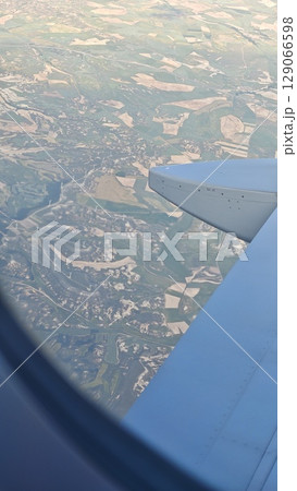 View from airplane window showing patchwork fields and landscapes far below the wing 129066598