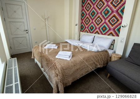 Interior of a spacious hotel bedroom with fresh linen on a big double bed. Cozy contemporary room in a modern house. Interior of a spacious hotel bedroom with fresh linen on a big double bed. Cozy contemporary room in a modern house. 129066828