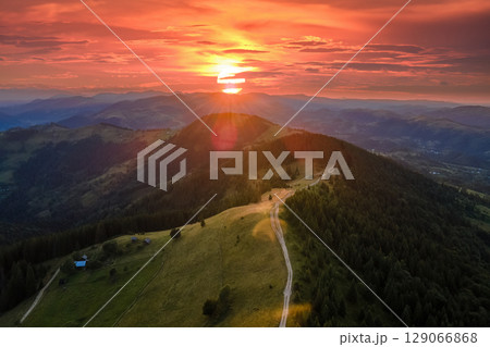 Hikers shelter on mountainside. Beautiful nature landscape. Aerial view of colorful sunset in wild mountains. Dark pine forest illuminated with bright setting sun 129066868