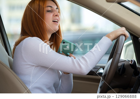 Happy redhead girl talking on her mobile phone behind the wheel driving a car. 129066888