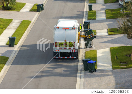 Garbage removal in residential area. Waste truck loading household rubbish while driving on suburban street 129066898