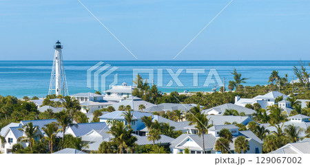 Expensive mansions between green palm trees in island small town Boca Grande in southwest Florida, USA. White lighthouse on sea shore for commercial vessels navigation 129067002