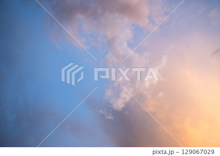 Dramatic moody sunset landscape with puffy clouds lit by yellow setting sun and blue sky. 129067029