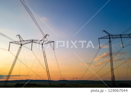Dark silhouette of high voltage towers with electric power lines at sunrise. 129067044