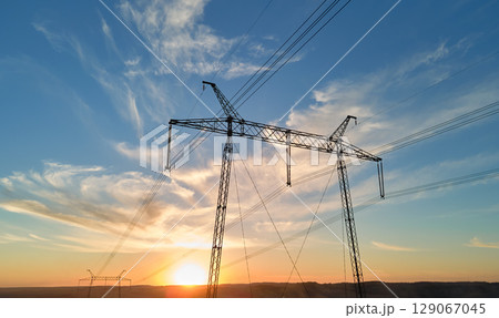 Dark silhouette of high voltage tower with electric power lines at sunrise. Transmission of electric energy concept 129067045