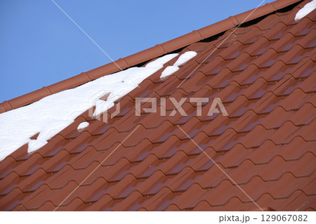 Closeup of house roof top covered with snow in cold winter. Tiled covering of building in wintertime weather 129067082