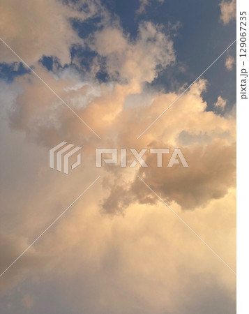 Vibrant clouds illuminated by warm sunset light, stunning sky scene filled with soft hues of orange, and gold. Peaceful and atmospheric nature background Vibrant clouds illuminated by warm sunset light, stunning sky scene filled with soft hues of orange, and gold. Peaceful and atmospheric nature background 129067235