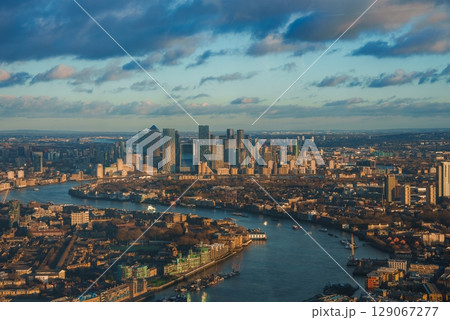 Aerial view of London's Canary Wharf skyline with modern skyscrapers. The River Thames reflects the warm glow of the setting sun during Christmas. 129067277