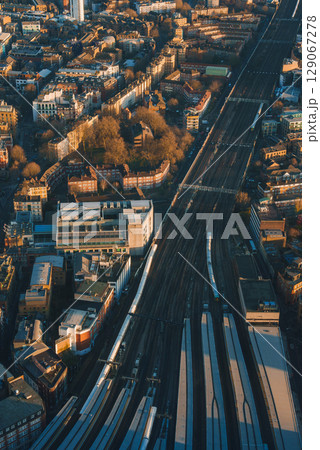 Aerial perspective of London's urban landscape with railway tracks, modern and historic buildings, and greenery, illuminated by warm, golden light. 129067278