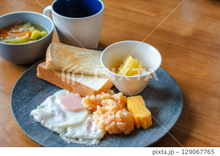 トーストと目玉焼き、明太ポテトやフルーツが並ぶ和洋ミックスの朝食 129067765