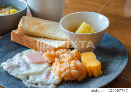 トーストと目玉焼き、明太ポテトやフルーツが並ぶ和洋ミックスの朝食 129067767