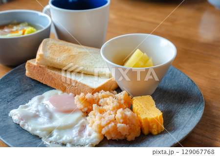 トーストと目玉焼き、明太ポテトやフルーツが並ぶ和洋ミックスの朝食 トーストと目玉焼き、明太ポテトやフルーツが並ぶ和洋ミックスの朝食 129067768