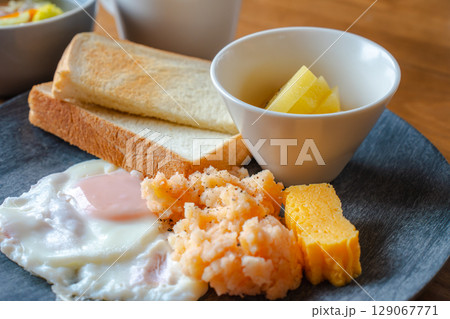 トーストと目玉焼き、明太ポテトやフルーツが並ぶ和洋ミックスの朝食 129067771
