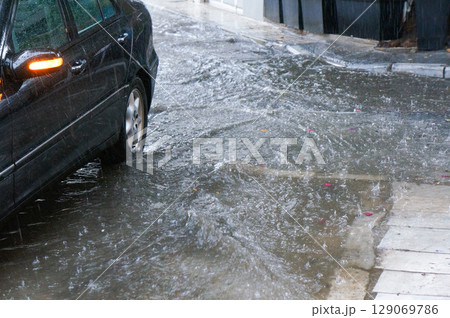 大雨で浸水し始める街中のとある道路 129069786