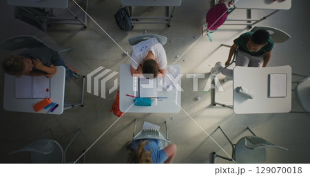 Sad Elementary School Student Sitting Alone at Desk and Crying While Classmates Bullying Him 129070018