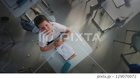 Depressed Primary School Boy Sitting at Desk, Looking at Camera While Aggressive Classmates Abusing Him 129070072