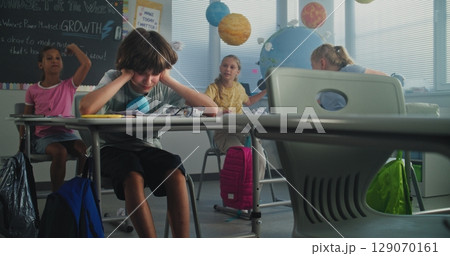 Depressed Primary School Boy Sitting at Desk While Classmates Abusing Him, Throwing Papers Depressed Primary School Boy Sitting at Desk While Classmates Abusing Him, Throwing Papers 129070161