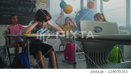 Depressed Primary School Boy Sitting at Desk While Classmates Abusing Him, Throwing Papers Depressed Primary School Boy Sitting at Desk While Classmates Abusing Him, Throwing Papers 129070163