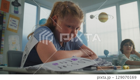 Upset Elementary School Girl Crying While Classmates Bullying Her, Laughing and Throwing Papers 129070169