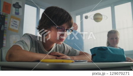 Sad Elementary School Student Sitting Alone and Crying While Classmates Bullying Him Sad Elementary School Student Sitting Alone and Crying While Classmates Bullying Him 129070271