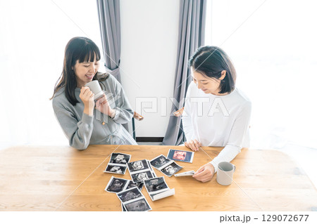 リビングでエコー写真を見ながら赤ちゃんが生まれてくるのを待ち望んでいる母と娘 リビングでエコー写真を見ながら赤ちゃんが生まれてくるのを待ち望んでいる母と娘 129072677