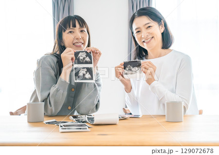 リビングでエコー写真を見ながら赤ちゃんが生まれてくるのを待ち望んでいる母と娘 129072678
