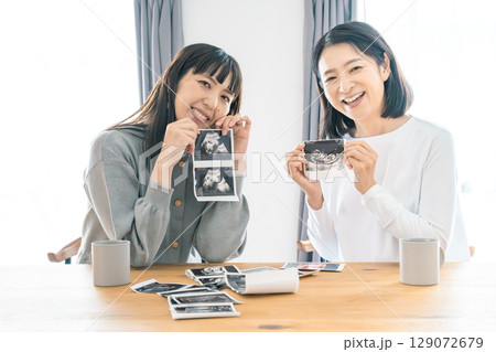 リビングでエコー写真を見ながら赤ちゃんが生まれてくるのを待ち望んでいる母と娘 リビングでエコー写真を見ながら赤ちゃんが生まれてくるのを待ち望んでいる母と娘 129072679